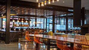 A modern dining area with a long table, orange chairs, and hanging light fixtures. - Canopy by Hilton Memphis Downtown (Memphis)