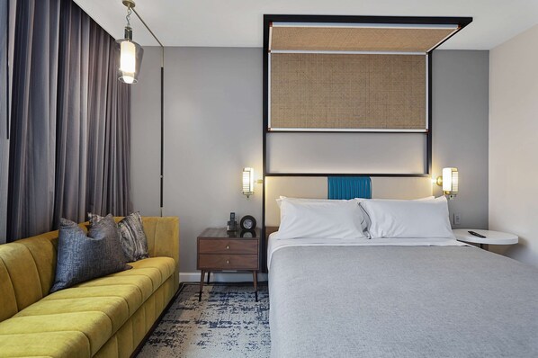 A hotel room with a bed, a sofa, a nightstand, and a wall-mounted headboard.