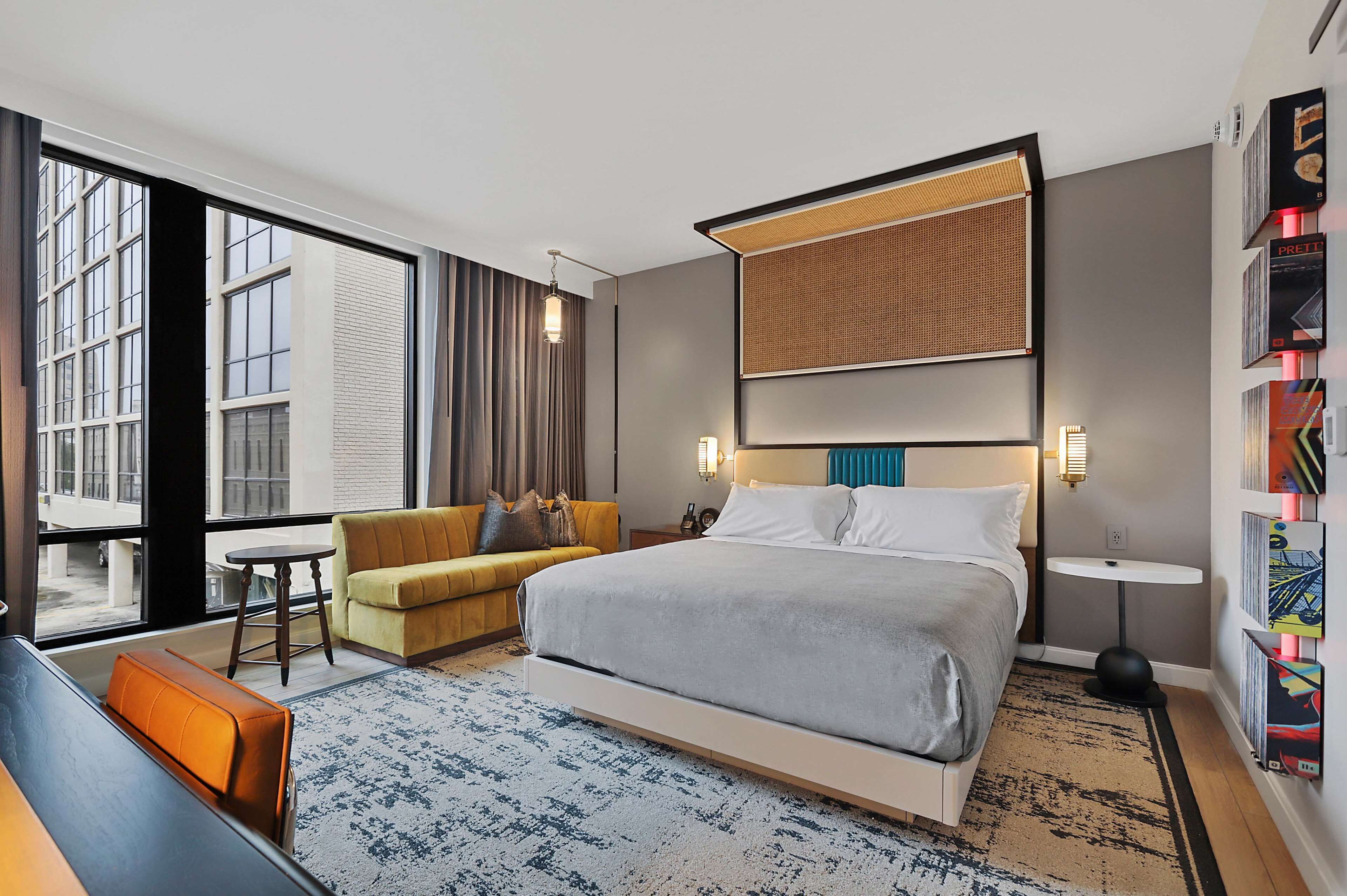 A modern hotel room with a large bed, a sofa, a small table, and a bookshelf.