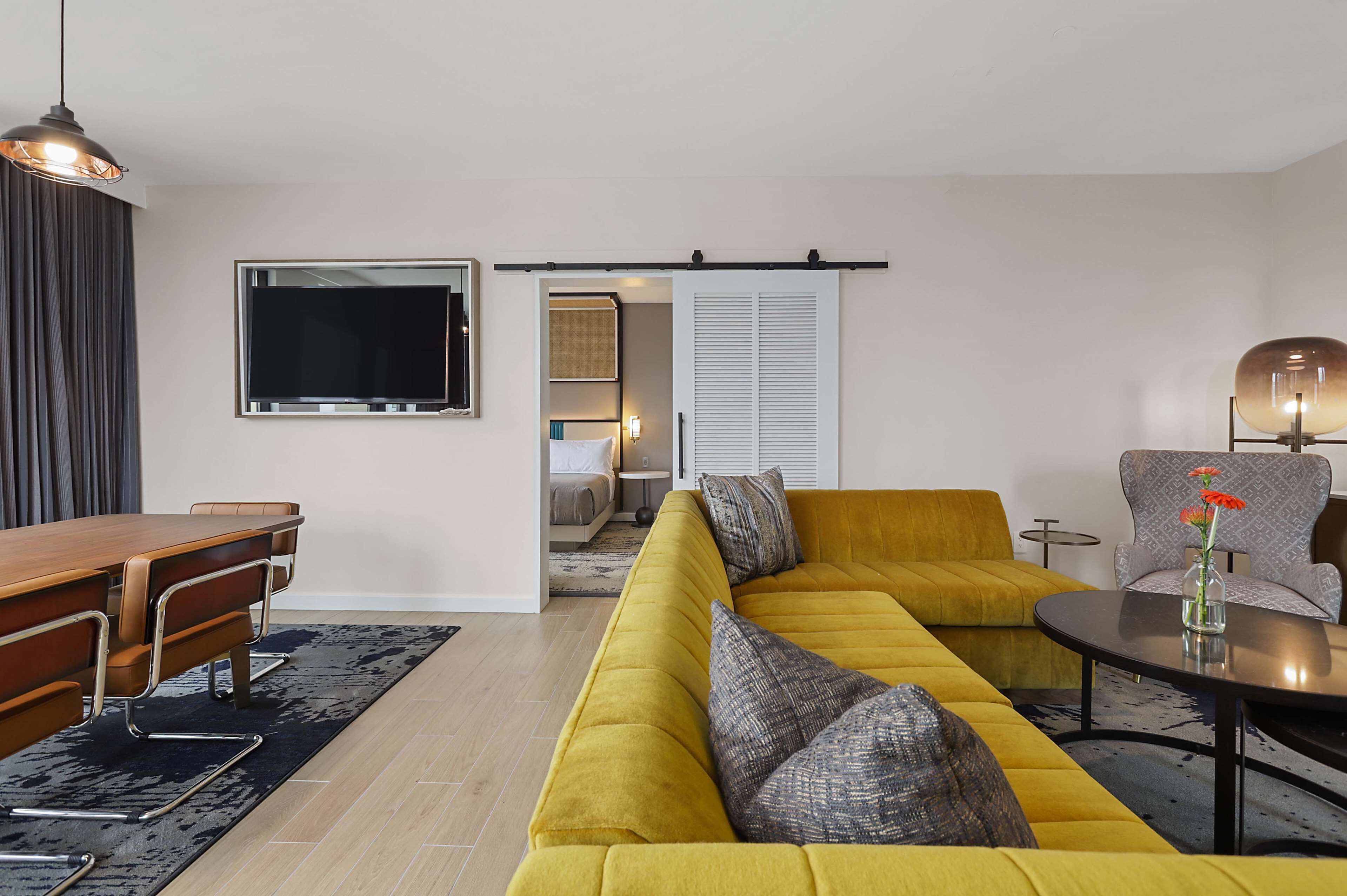 Un salon moderne avec un canapé jaune, une table à manger en bois et un téléviseur fixé au mur.