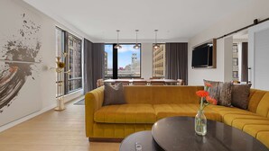 A modern living room with a mustard yellow sofa, a round coffee table, and a large window offering a city view. - Canopy by Hilton Memphis Downtown (Memphis)