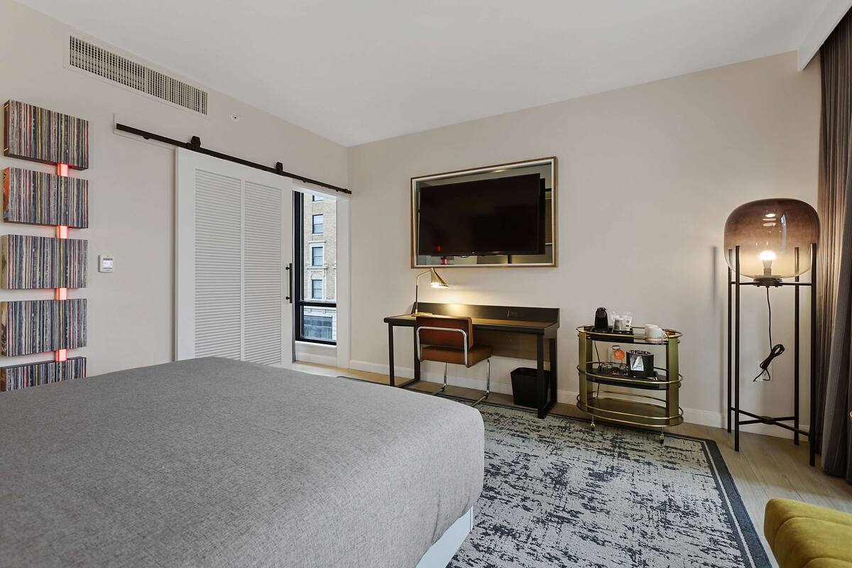 Une chambre d’hôtel équipée d’un lit, d’un bureau, d’une télévision, d’une bibliothèque et d’une lampe de sol.