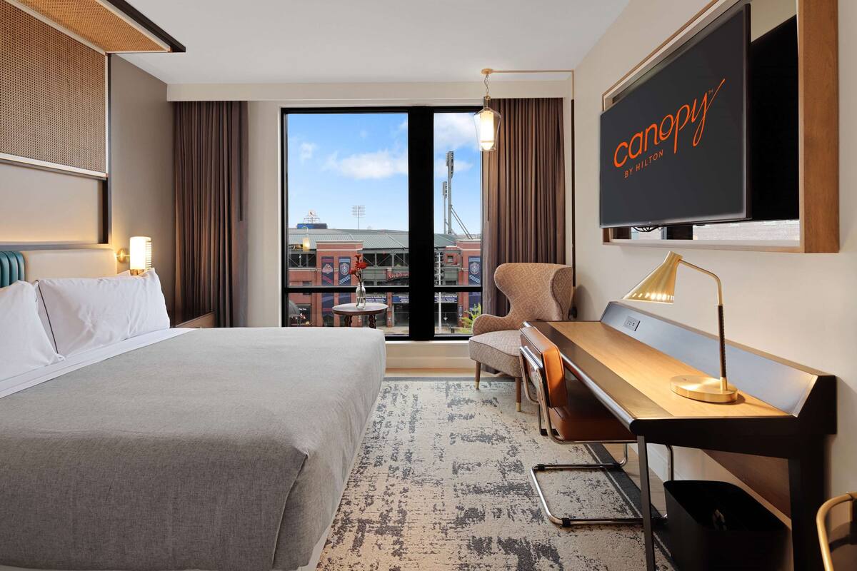 Une chambre d’hôtel équipée d’un lit, d’un bureau, d’une chaise et d’un grand écran de télévision affichant le nom de l’hôtel.