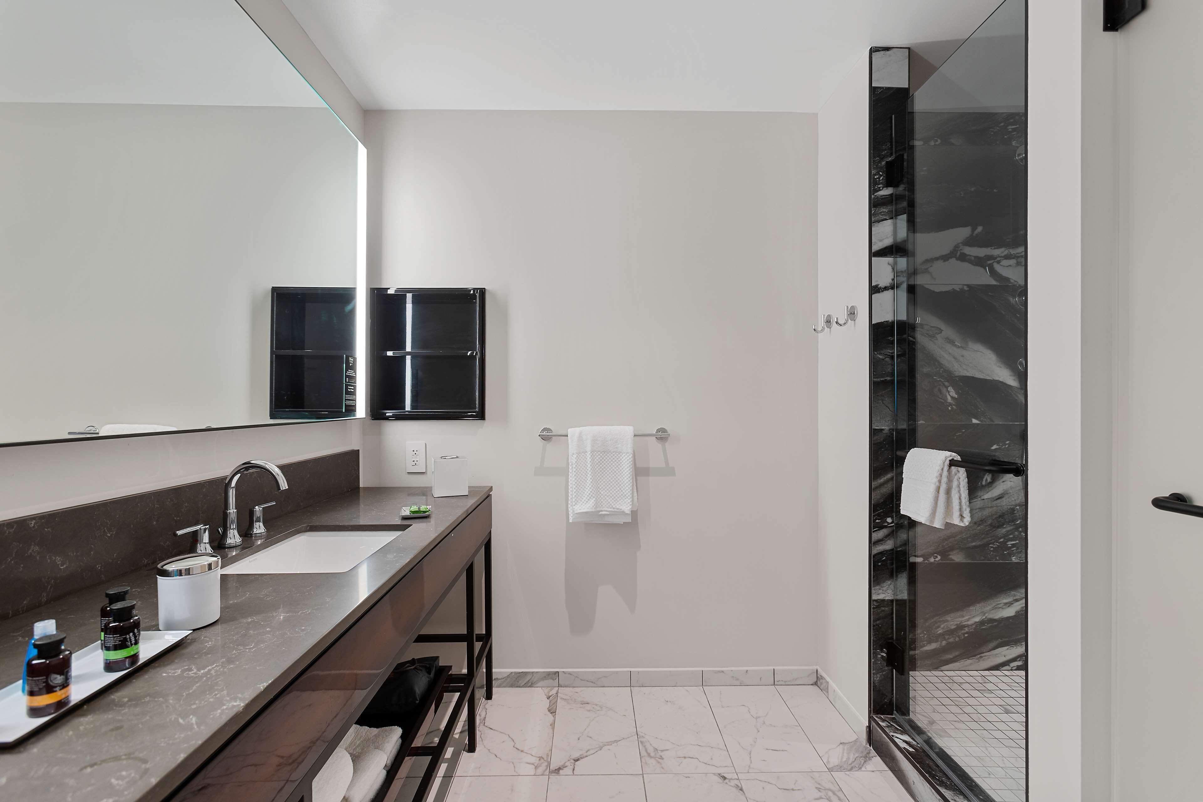 Une salle de bain moderne avec un grand miroir, deux lavabos, un meuble-lavabo et une douche à parois de verre.