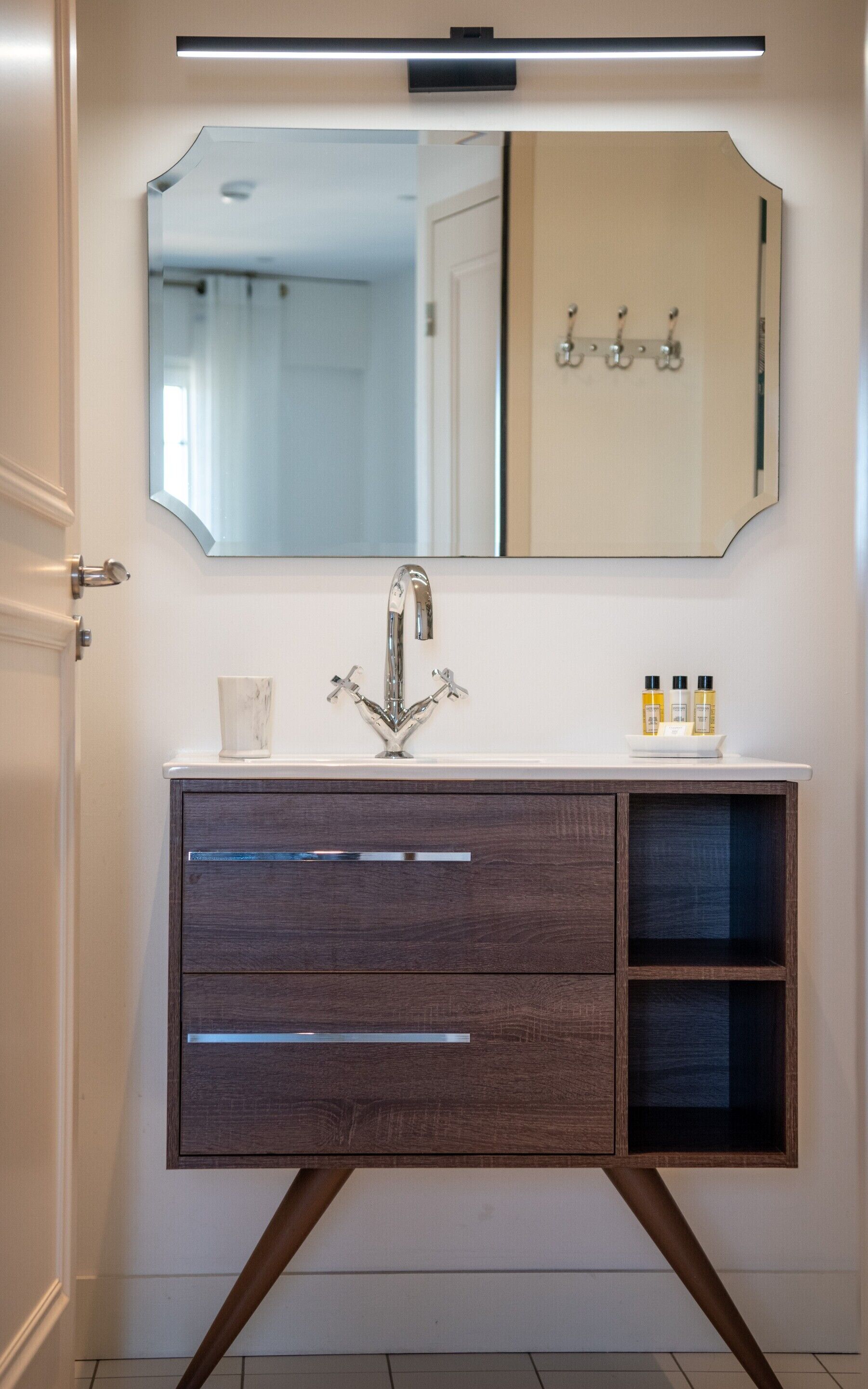 A bathroom with a modern vanity, a large mirror, and a wall-mounted light fixture.