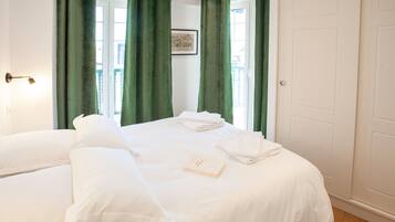 Habitación de hotel con dos camas, cortinas verdes, un cuadro en la pared y un libro sobre la cama.