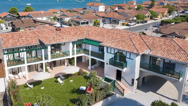 A coastal residential area with a two-story house featuring a balcony, a small lawn, and a view of the sea.