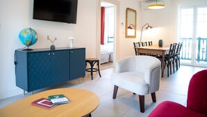 A modern living room with a flat-screen TV, a globe on a cabinet, a dining area with a table and chairs, and a balcony with a railing.