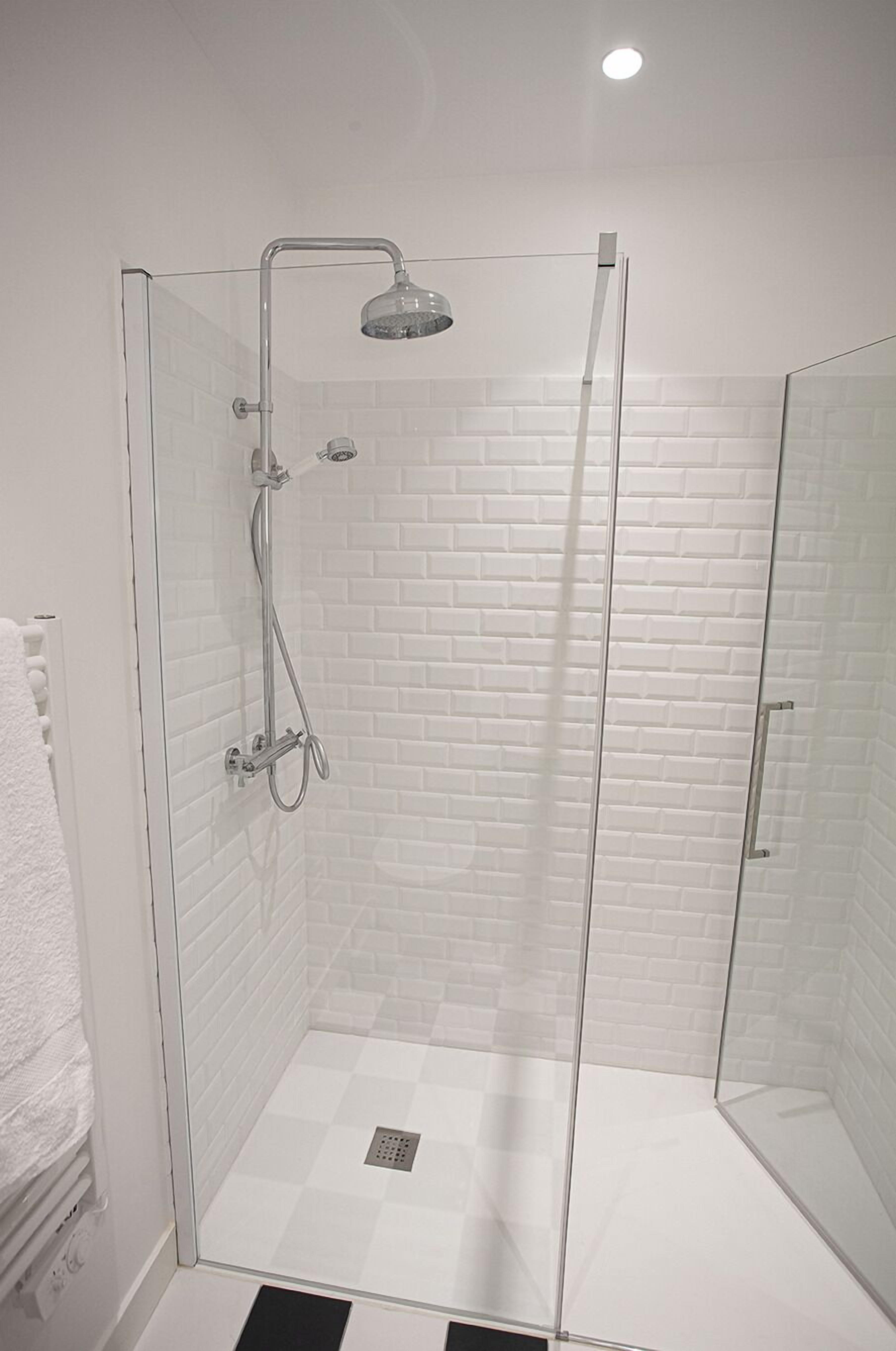 A glass-enclosed shower with a white brick wall and a white floor.
