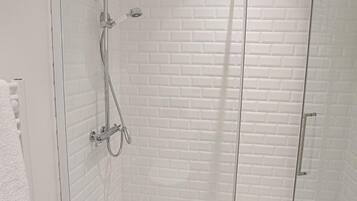 A glass-enclosed shower with a white brick wall and a white floor.