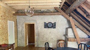A rustic dining room with wooden beams, a stone wall, and a chandelier.