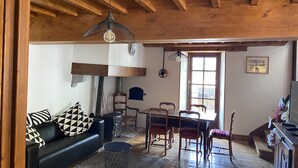 A cozy living room with a black leather sofa, a dining table with wooden chairs, and a wooden ceiling.