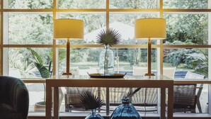 Une pièce avec une table en verre, deux lampes et une vue sur la verdure à l’extérieur.