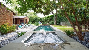 Une piscine rectangulaire agrémentée d’une cascade, entourée d’une terrasse en briques et de chaises longues.