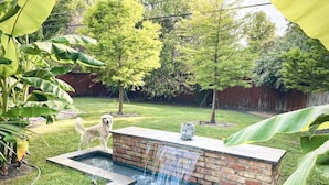 Un jardin avec une petite fontaine en briques et un chien.