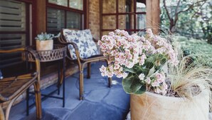 Une véranda en bois avec des meubles en osier, un pot de fleurs orné de fleurs roses et une vue sur les arbres.