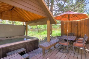 Een houten terras met een jacuzzi, buitenmeubels en een overdekt gedeelte met een parasol.