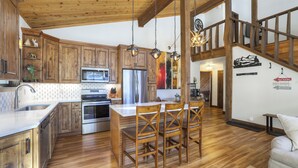 A spacious kitchen with wooden cabinets, stainless steel appliances, and a central island with chairs. - Dog Friendly, On Shuttle Route, Private Hot Tub, Near River, Walk to Town (Breckenridge)