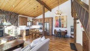 A spacious living area with a stone fireplace, wooden ceiling beams, and a dining area with a large table and chairs. - Dog Friendly, On Shuttle Route, Private Hot Tub, Near River, Walk to Town (Breckenridge)