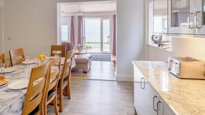 A modern kitchen with a marble countertop, a built-in oven, and a toaster. There is a dining area with wooden chairs and a table set for two. - Beachside, West Yardley House - UK31200 (Downderry and Seaton, near Looe)