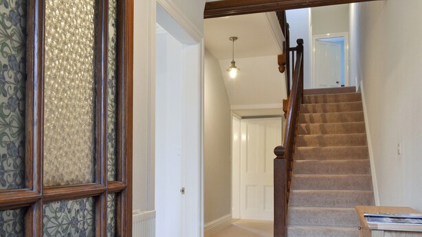 A hallway with a wooden door, a radiator, a staircase, and a small table. - 4 bedroom accommodation in Keswick (Keswick)
