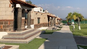 A building with a series of arches and columns, a tiled pathway, and a grassy area with palm trees. - Hotel Villas Mahando (Ezequiel Montes)