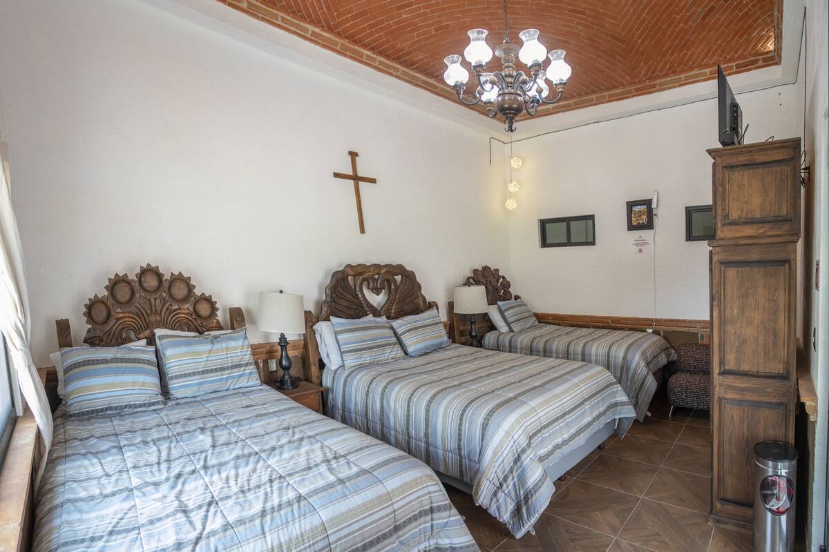 A room with three beds, a wooden ceiling, a cross on the wall, and a chandelier.