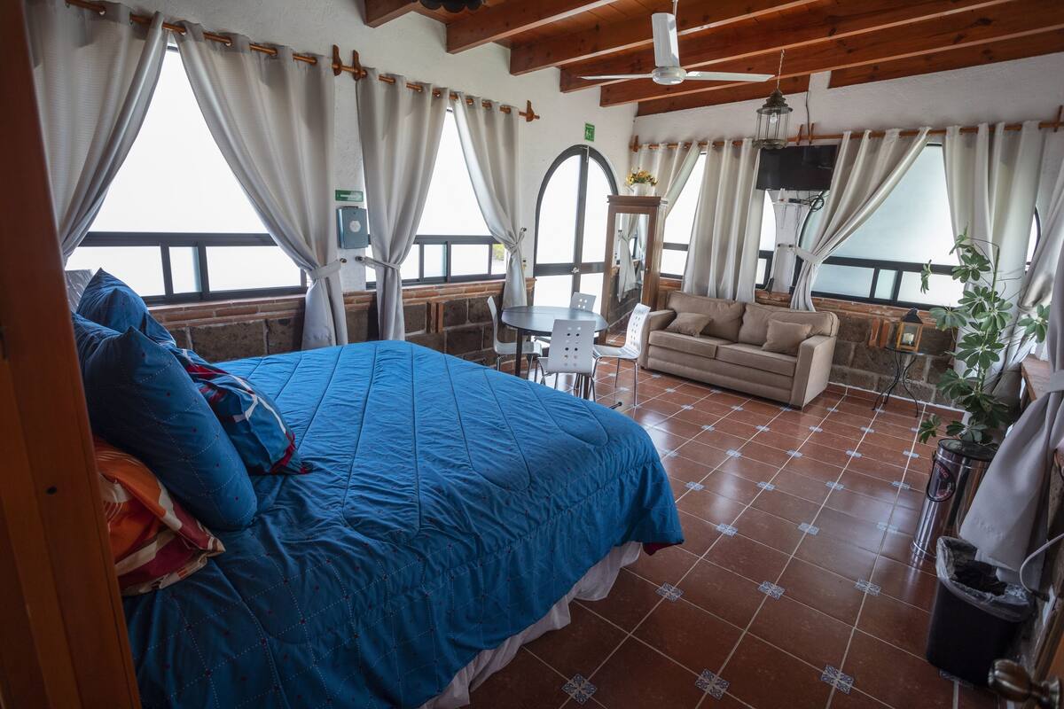 A bedroom with a large bed, a sofa, a small table, and a TV.