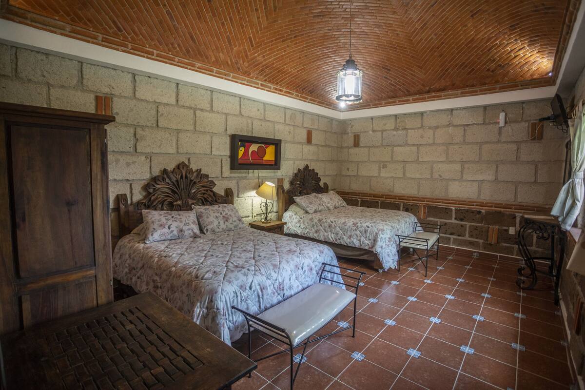 A room with two beds, a wooden cabinet, a bench, and a tiled floor.