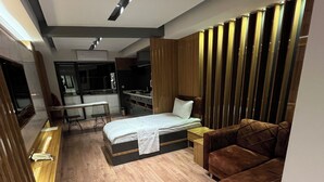 Una habitación moderna con cama, sofá, piso de madera y una zona de cocina al fondo.