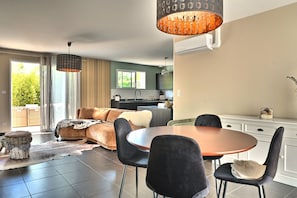 A modern living room with a sofa, dining table, chairs, and a kitchen in the background.
