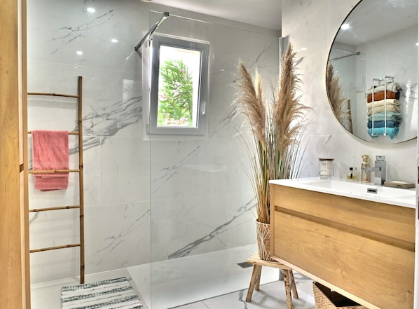 A modern bathroom with a shower, a vanity with a mirror, and a window.