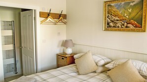 Une chambre à coucher avec un lit, des oreillers, une table de chevet avec une lampe, un tableau au mur et une porte avec un porte-serviettes.