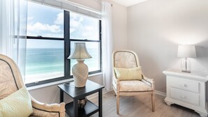 Une pièce dotée d’une grande fenêtre donnant sur l’océan, d’un fauteuil avec un coussin, d’une petite table avec une lampe et d’une table de chevet avec une lampe.