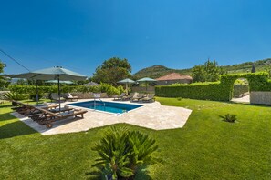 Un jardin avec une piscine, des chaises longues et des parasols.
