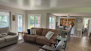 A spacious living room with a brown sofa, a beige armchair, and a patterned rug. There is a dining area with a wooden table and chairs, and a kitchen visible through an open door. - Ultimate Family Lake Retreat w/ Swim Slide, Sandy bottom, and Bar/TV Lounge (Holcombe)
