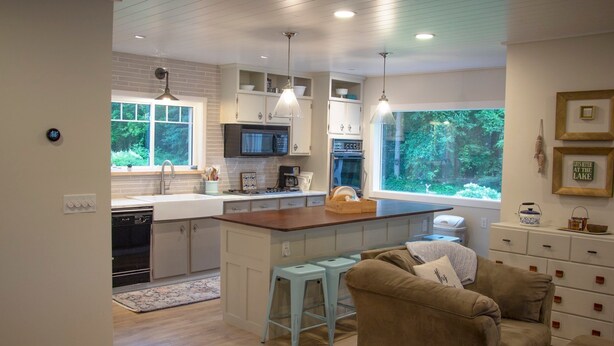 A modern kitchen with a central island, bar stools, a built-in oven, and a large window offering a view of the outdoors. - Ultimate Family Lake Retreat w/ Swim Slide, Sandy bottom, and Bar/TV Lounge (Holcombe)