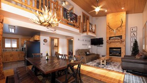 A spacious living area with a wooden dining table, chairs, a sofa, and a fireplace. - Summit Trails Lodge: Cozy, Hot Tub, Trail Access (Lead)