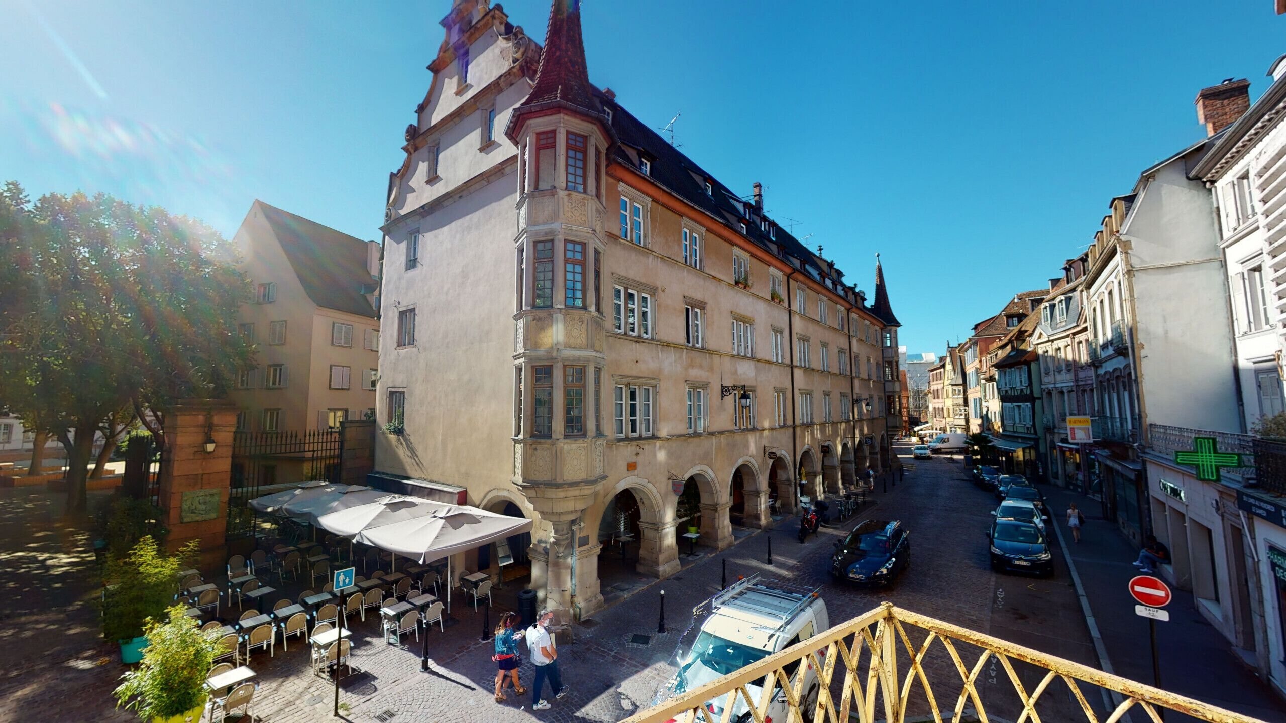 A historic building with a prominent tower, a courtyard with outdoor seating, and a cobblestone street.