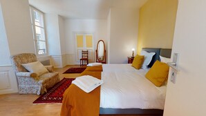 Ein Hotelzimmer mit Bett, Sessel, Spiegel, kleinem Tisch mit Lampe und Tür.