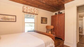 A bedroom with a wooden bed, a chair, a wardrobe, and a window with a floral valance.