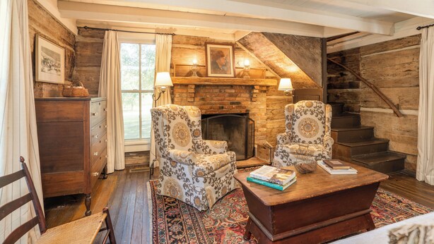A cozy room with a fireplace, two patterned armchairs, a wooden coffee table, and a staircase. - The Holly House at Green Frog Farm (Alamo)
