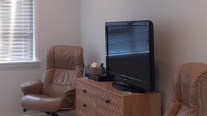 Et værelse med to læderlænestole, et træskab med et fladskærms-tv og en aircondition-enhed på væggen.