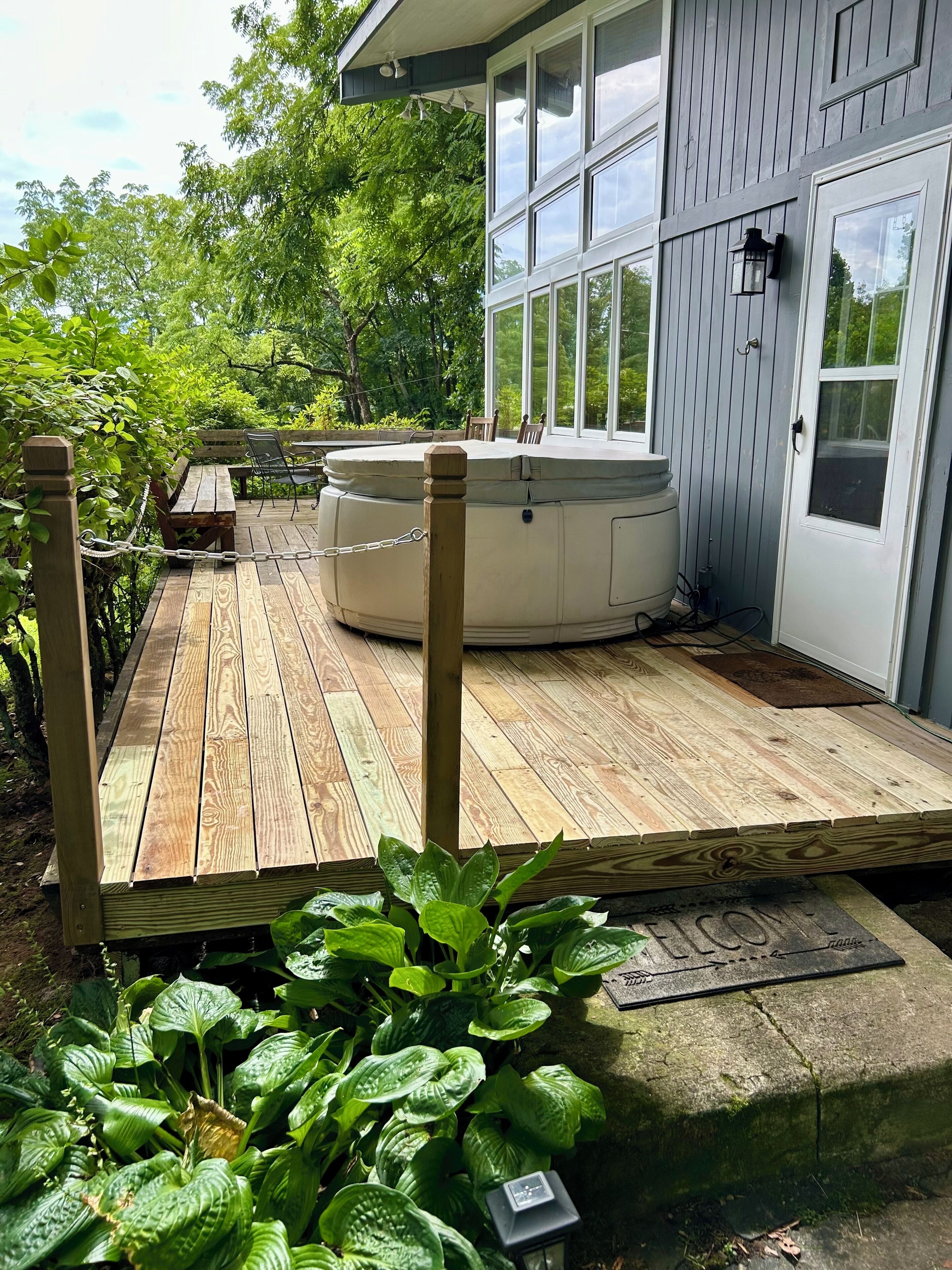 En træterrasse med jacuzzi, bænk og dør med et vindue.