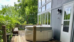 Una terraza de madera con un jacuzzi, un banco y una puerta con ventanal.