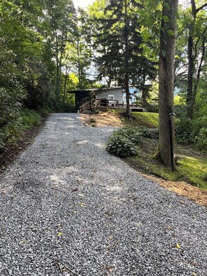 A gravel driveway leading to a cabin with a deck and outdoor seating area surrounded by trees.