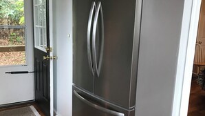 Un refrigerador de acero inoxidable en una cocina con suelo de madera y una puerta blanca.