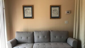 A grey sectional sofa against a beige wall with two framed artworks above it.
