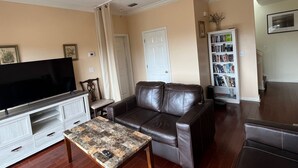 A living room with a television, leather sofa, a coffee table, a ceiling fan, and a bookshelf.