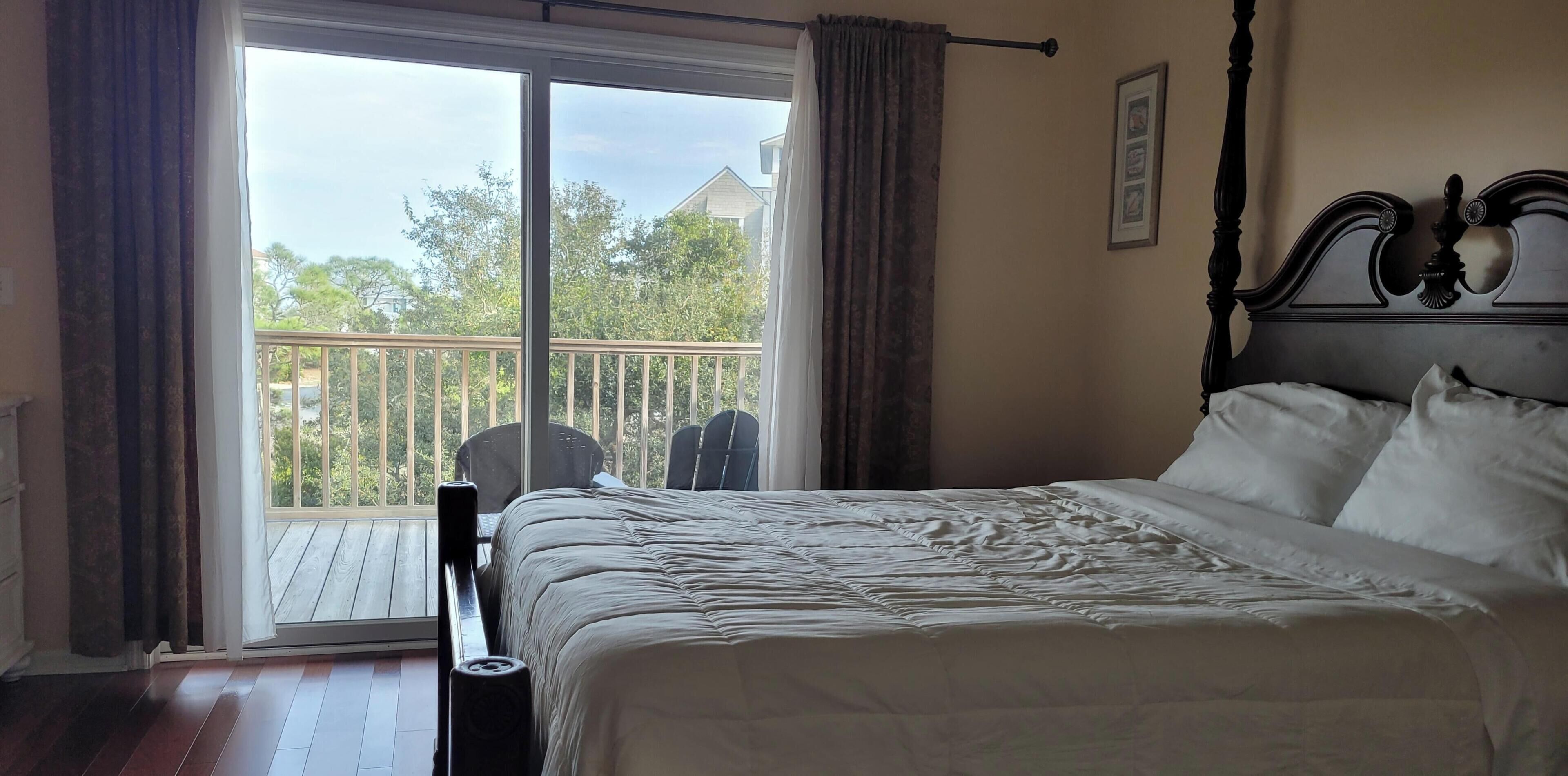 Un dormitorio con cama, ventana con cortinas, balcón y una silla.